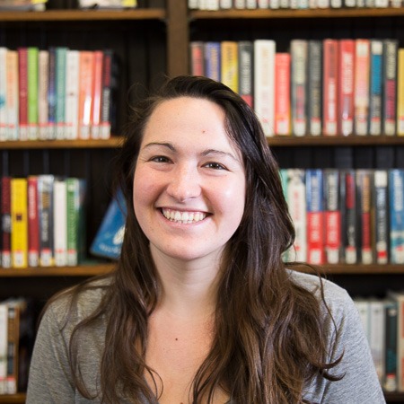 Tess Wilson is photographed in front of bookshelves in a library.